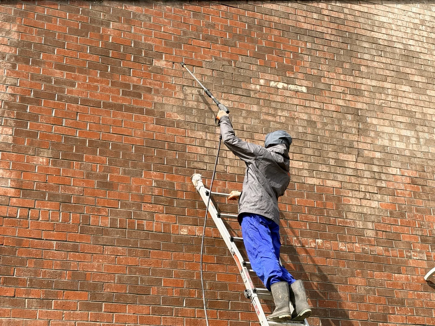 Worker cleaning a brick wall from a ladder