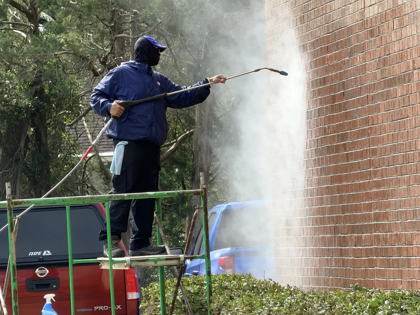 Worker pressure washing the exterior of a brick building from an elevated platform